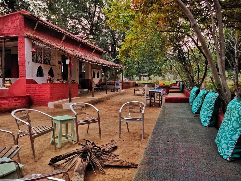 Rustic brick and mud cottage courtyard with bonfire setup, sit-out verandah, and garden seating at Bhoramdeo Jungle Retreat