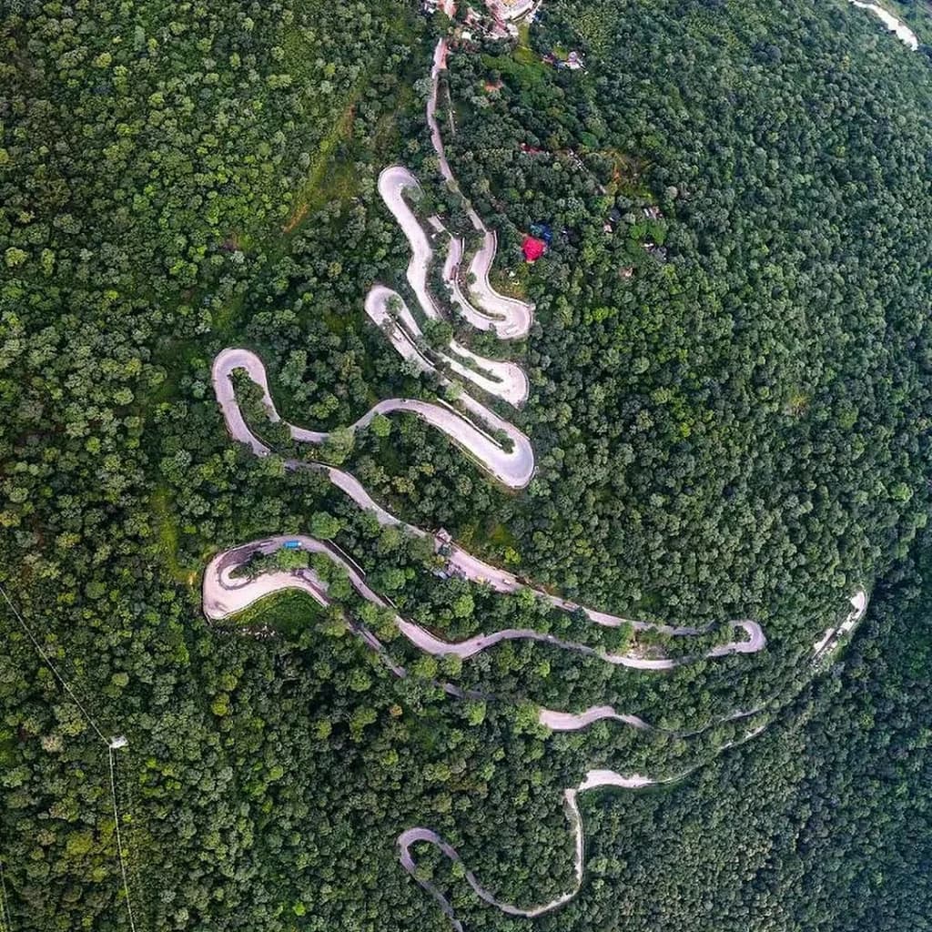 Aerial view of winding serpentine hairpin bends through the lush green forests of Chilfi Ghati Kawardha